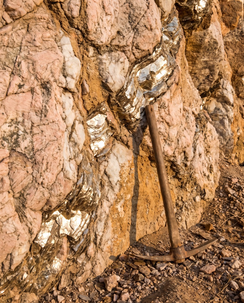 A mine face of pale pegmatite rock with veins of mica